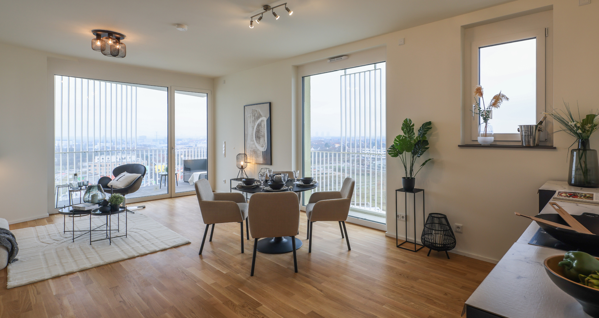 KI-basierte Bildbeschreibung: Modernes, helles Apartment mit großen Fenstern, Holzböden, einem runden Esstisch mit vier Stühlen, einem gemütlichen Wohnbereich mit Sesseln, Grünpflanzen und Stadtblick nach draußen.