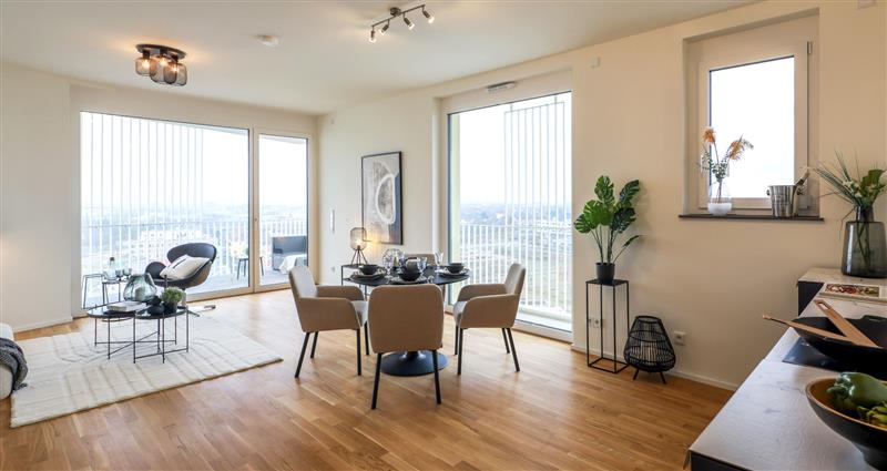 KI-basierte Bildbeschreibung: Eine helle, moderne Wohnung im Hochpunkt H mit großen Fenstern, hellem Holzboden, einem Esstisch für vier Personen, einer gemütlichen Sitzecke, Topfpflanzen, minimalistischem Dekor und Stadtblick durch die Fenster.